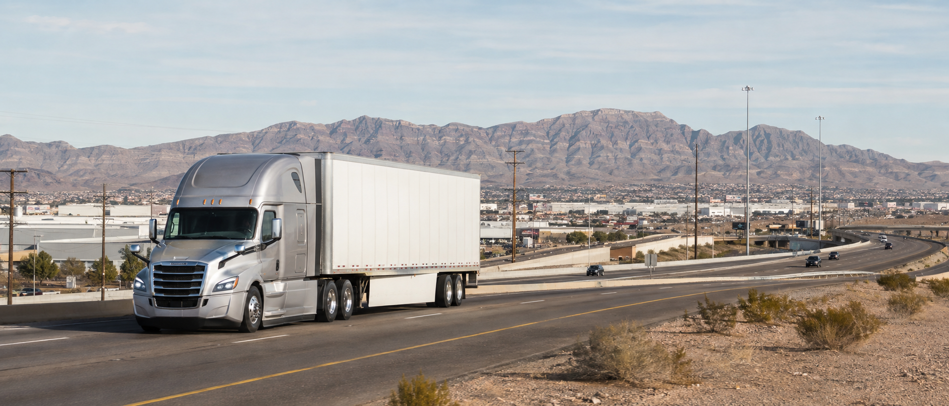 Generic silver tractor-trailer on an El Paso freight corridor with mountains beyond